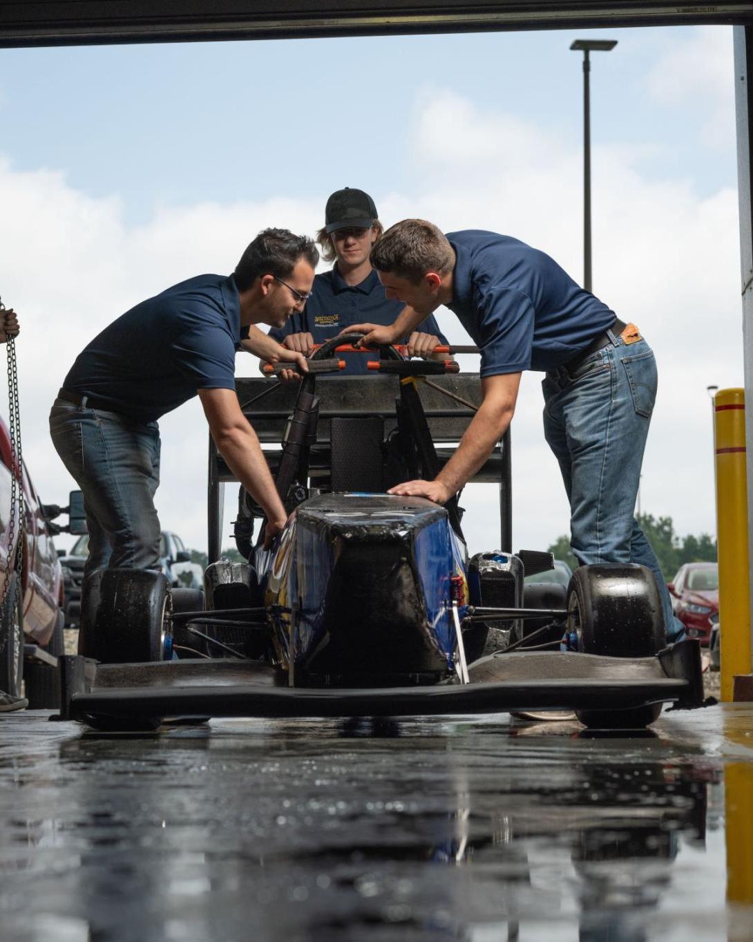 Three Kettering students examine a formula-style racing car inside the SAE Garage